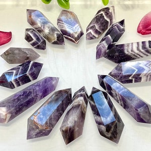 May include: A collection of 12 amethyst points with purple and white stripes. The points are arranged in a circle on a white surface.