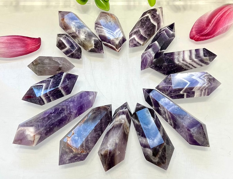 May include: A collection of 12 amethyst points with purple and white stripes. The points are arranged in a circle on a white surface.