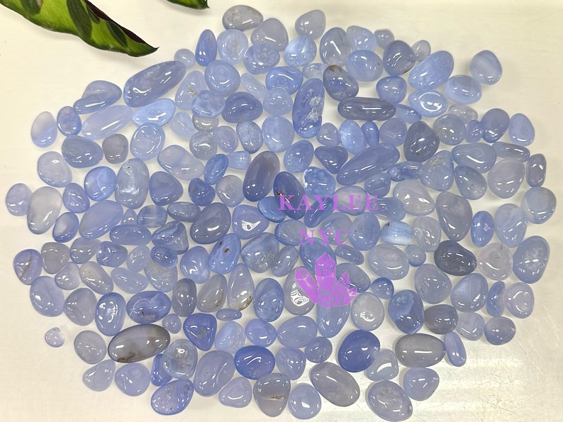 May include: A large collection of light blue chalcedony tumbled stones. The stones are smooth and polished, and they have a variety of shapes and sizes.