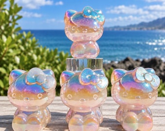May include: Four iridescent, translucent Hello Kitty figurines with a pearlescent finish. One figurine is elevated on a clear cylindrical stand, while three others are positioned in front on a flat surface, each featuring a bow.