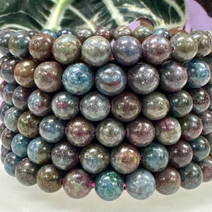 May include: A bracelet made of round, polished gemstone beads. The beads are a mix of colors, including blue, green, brown, and purple. The bracelet is stacked and appears to be made of multiple strands of beads.