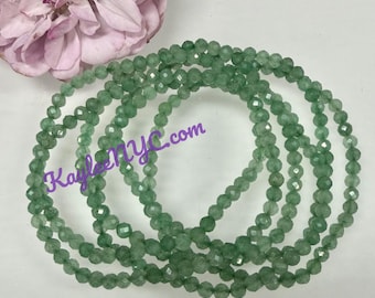 Puede incluir: Varias hebras de cuentas de piedras preciosas facetadas de color verde claro están dispuestas en un patrón circular. Una gran flor rosa suave está en la esquina superior izquierda. El texto "KayleeNYC.com" es visible en la imagen.