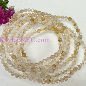 May include: A strand of golden rutilated quartz beads. The beads are faceted and have a translucent, golden color. The beads are strung on a clear elastic cord.