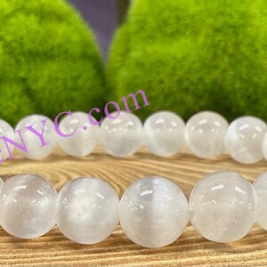 Puede incluir: Pulsera de cuentas de piedra lunar blanca con un acabado liso y pulido. Las cuentas son redondas y tienen un brillo sutil.