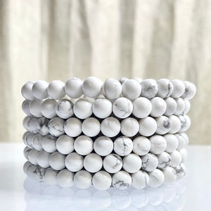 May include: A stack of white howlite bead bracelets. The beads are round and have a smooth, polished finish.