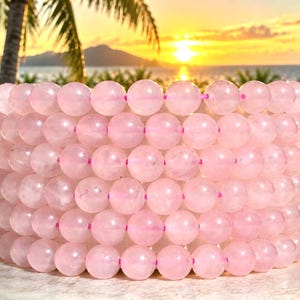 May include: A stack of six circular bracelets made of smooth, polished, light pink rose quartz beads. Each bead is spherical and uniform in size, strung together on a thin, bright pink elastic cord that is visible between the beads.