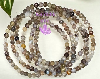 Puede incluir: Un conjunto de seis pulseras hechas con cuentas de ágata veteada en marrón, blanco y gris. Las pulseras están apiladas unas sobre otras.