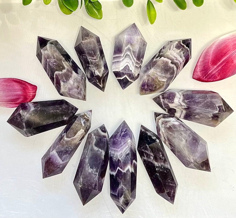 May include: A collection of ten amethyst crystal points, each with a unique purple and white banded pattern. The points are arranged in a circle on a white surface.