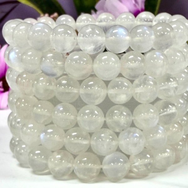 May include: A stack of five beaded bracelets made of translucent, round, white moonstone beads. Each bracelet features polished, spherical stones with a subtle iridescent sheen, arranged in a uniform circular pattern to form a cylindrical shape.