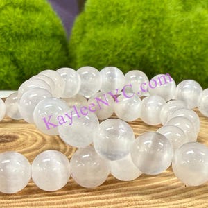 Puede incluir: Dos pulseras de piedras blancas con cuentas redondas. Las pulseras est&aacute;n hechas de piedra lunar blanca y est&aacute;n apiladas una encima de la otra. Las pulseras est&aacute;n sobre una superficie de madera.