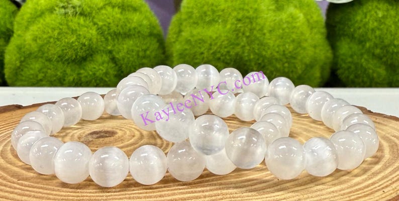 Puede incluir: Dos pulseras de piedras blancas con cuentas redondas. Las pulseras est&aacute;n hechas de piedra lunar blanca y est&aacute;n apiladas una encima de la otra. Las pulseras est&aacute;n sobre una superficie de madera.