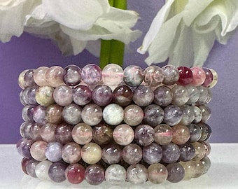Op de afbeelding: Een stapel van acht armbanden gemaakt van kleine, ronde, veelkleurige kralen. De kralen zijn doorschijnend en hebben een gevlekt uiterlijk. De kleuren van de kralen omvatten roze, paars, wit en groen.