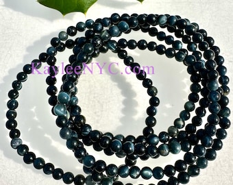Pode incluir: Um conjunto de quatro pulseiras de contas de olho de tigre azul. As contas são redondas e têm uma cor azul escura com um brilho sutil.