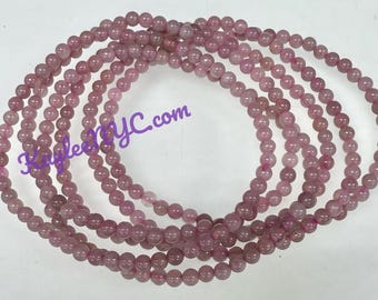 Puede incluir: Varios hilos de cuentas de piedras preciosas rosas, cada una con un tamaño y forma consistentes. Las cuentas son de un color rosa suave y apagado, y la imagen está bien iluminada, resaltando la textura suave de las piedras. El texto "RayleesNYC.com" es visible.