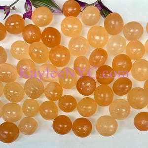May include: A collection of approximately 40 smooth, round, orange carnelian tumbled stones. The stones are various sizes and shapes, with a natural, polished finish.