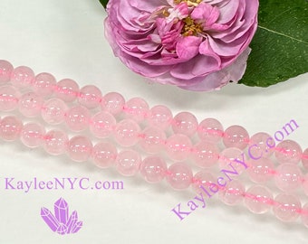 Può includere: Una collana di perle di quarzo rosa. Le perle sono rotonde e traslucide, con una leggera sfumatura rosa. Le perle sono infilate su un filo trasparente. Le perle sono disposte in un mucchio sciolto, con alcune perle che si sovrappongono. Le perle sono fotografate su uno sfondo bianco.