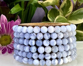 May include: A bracelet made of light blue agate beads. The beads are round and have a smooth, polished finish. The bracelet is strung on a brown leather cord.