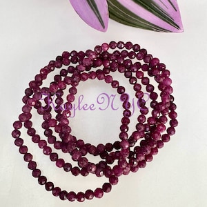 May include: A strand of deep purple faceted gemstone beads. The beads are strung on a clear elastic cord and are approximately 6mm in diameter.