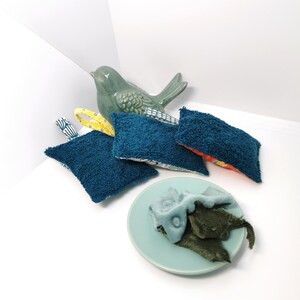 May include: Four blue and white patterned dishcloths with a yellow trim and a green ceramic bird figurine. The dishcloths are folded and arranged on a white surface.