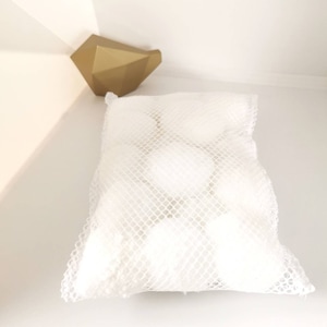 Peut inclure: Un sac à linge en maille blanche rempli de boules blanches. Le sac est sur une surface blanche.