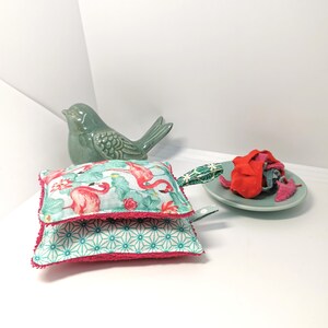 May include: Two pink and green dishcloths with a flamingo print and a geometric pattern. The dishcloths have a pink trim and a green loop handle.