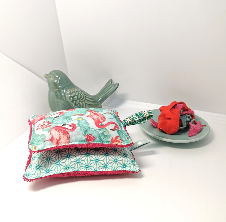 May include: Two pink and green dishcloths with a flamingo print and a geometric pattern. The dishcloths have a pink trim and a green loop handle.
