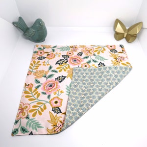 May include: A pink and white fabric placemat with a floral pattern and a green and white geometric pattern on the reverse.