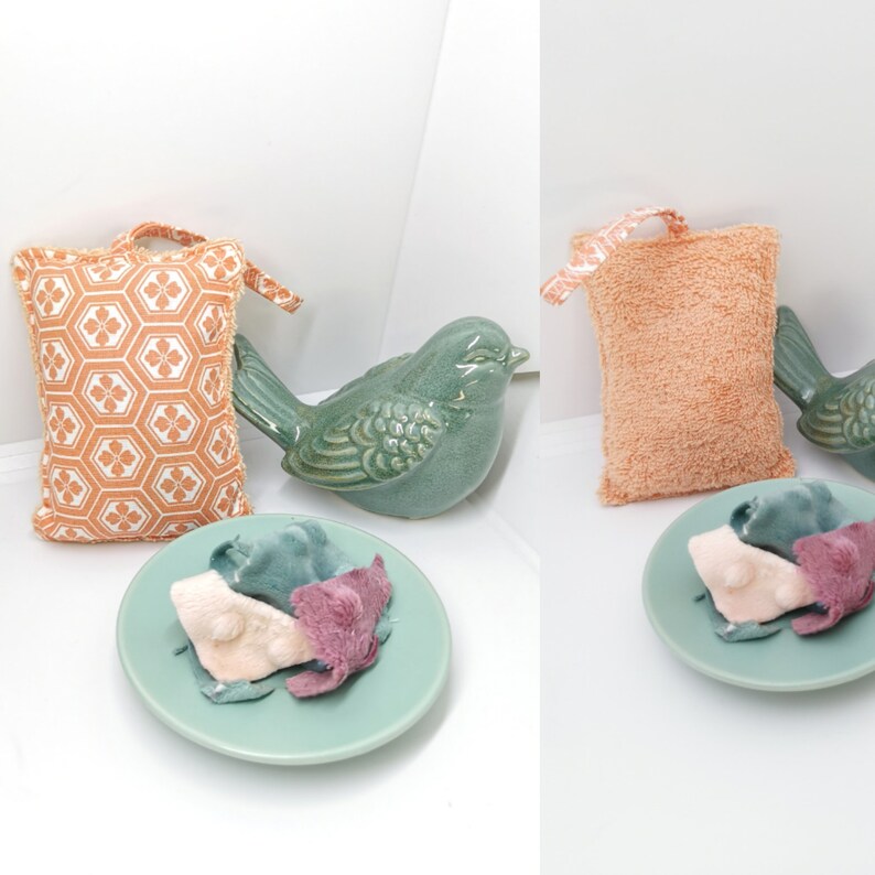 May include: Two decorative bath poufs, one orange and white with a geometric pattern and one peach coloured, are displayed on a white surface. A green ceramic bird figurine is in the background.