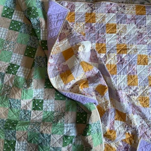 May include: Two handmade quilts with patchwork designs. One quilt features squares of green, white, and tan fabrics. The other quilt has squares of yellow, purple, and white fabrics. Both quilts are folded and have a quilted pattern.