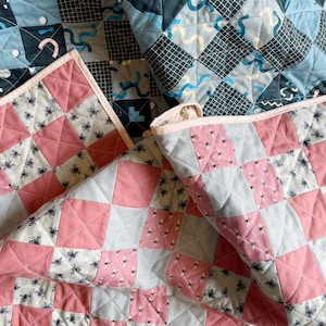 May include: Two quilts made with different fabrics. One quilt is pink and gray with a pattern of bees. The other quilt is blue and black with a geometric pattern.
