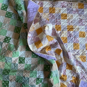 Pu&ograve; includere: Due trapunte fatte a mano con disegni patchwork. Una trapunta presenta quadrati di tessuti verdi, bianchi e beige. L'altra trapunta ha quadrati di tessuti gialli, viola e bianchi. Entrambe le trapunte sono piegate e hanno un motivo trapuntato.