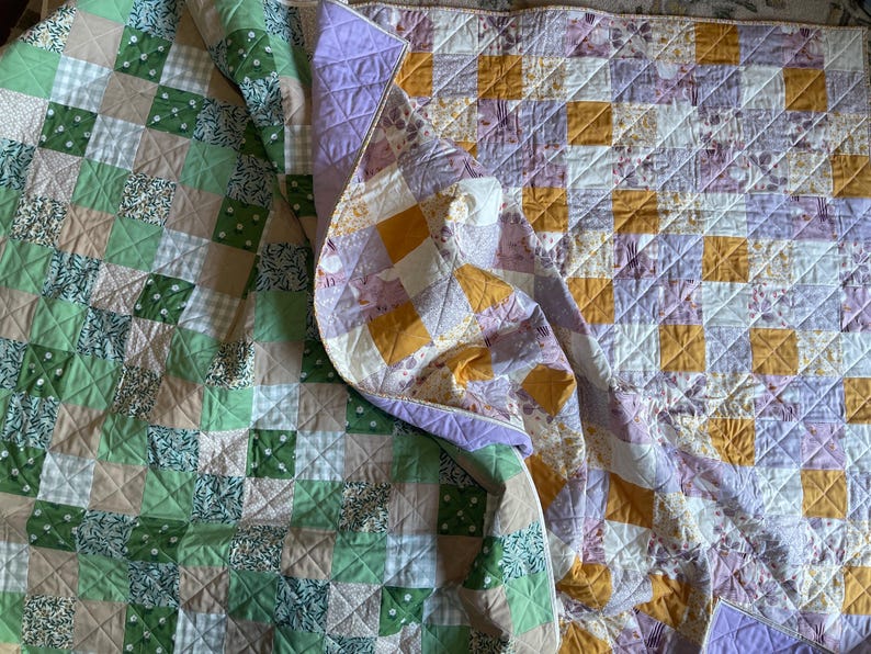 Pu&ograve; includere: Due trapunte fatte a mano con disegni patchwork. Una trapunta presenta quadrati di tessuti verdi, bianchi e beige. L'altra trapunta ha quadrati di tessuti gialli, viola e bianchi. Entrambe le trapunte sono piegate e hanno un motivo trapuntato.