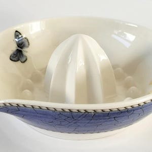 May include: A white ceramic citrus juicer with a built-in reamer. The bowl has a blue cracked pattern around the rim and a butterfly design. The juicer is designed for squeezing citrus fruits.