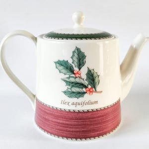 May include: White ceramic teapot with a green and red holly design and the text "Ilex aquifolium". The teapot has a red and white striped band around the bottom.