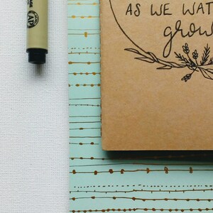 May include: A brown notebook with a light blue patterned cover. The notebook has a circle on the front with the text "Letters to my daughter as we grow".