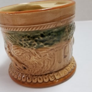 May include: A brown ceramic mug with a green and brown design. The mug has a raised design of a tree and a bird.
