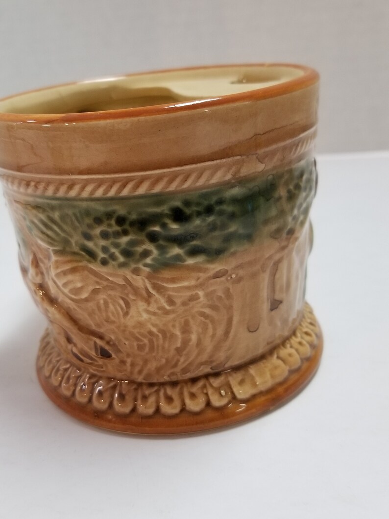 May include: A brown ceramic mug with a green and brown design. The mug has a raised design of a tree and a bird.