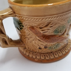 May include: A brown ceramic mug with a tree branch handle and a deer design. The mug has a brown glaze with green accents.