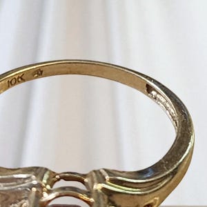 May include: Close-up of a gold ring with a decorative design. The ring is marked "10K" on the inside band. The ring has a classic, elegant style, suitable for various occasions. The ring's design includes a central stone setting.