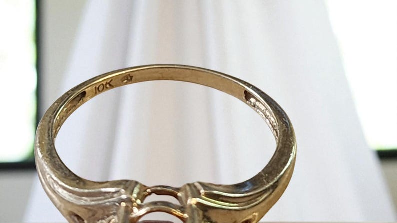 May include: Close-up of a gold ring with a decorative design. The ring is marked "10K" on the inside band. The ring has a classic, elegant style, suitable for various occasions. The ring's design includes a central stone setting.