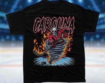 May include: Black t-shirt with a graphic of a skeleton hockey player in a red and white jersey, holding a hockey stick and skating in a tornado of fire. The text "CAROLINA" is above the player.