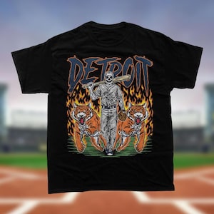 May include: Black t-shirt with a graphic of a skeleton baseball player holding a bat with the word "DETROIT" above him. The player is standing in front of two tigers with flames behind them.