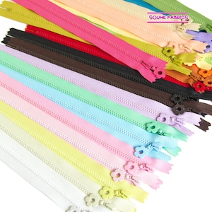 Puede incluir: Una colección de cremalleras coloridas en varios tonos, incluyendo blanco, amarillo, rosa, azul y verde. Cada cremallera presenta un tirador en forma de flor. El texto "SOUHE FABRICS" es visible en la esquina superior derecha.