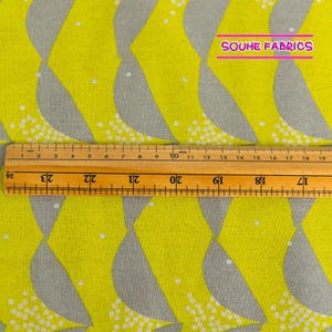 May include: A close-up of yellow fabric with a repeating pattern of gray stylized birds. The fabric is measured with a ruler that shows 24 centimeters.