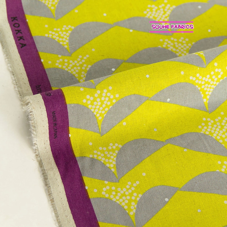 May include: Yellow fabric with a gray and white geometric pattern. The fabric has a white polka dot pattern on a gray background. The fabric is folded in half and the text "KOKKA" and "SOUHE FABRICS" is visible.