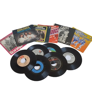 Könnte beinhalten: Eine Sammlung von Vintage-Schallplatten, darunter 45-RPM-Singles und Albumcover. Die Albumcover zeigen verschiedene Künstler und Titel, wie "Bee Gees Stayin' Alive" und "The Night Chicago Died". Die Schallplatten sind schwarz mit farbigen Etiketten.