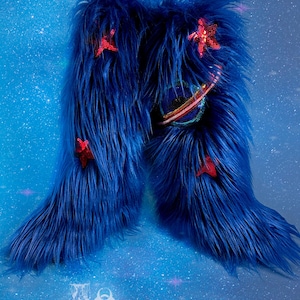 May include: A pair of bright blue faux fur boots. The boots are decorated with red sequined starfish and a colourful planet design. The boots have a long, shaggy texture against a starry blue background.