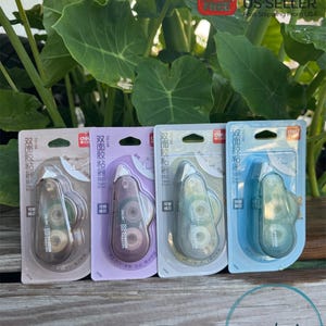 May include: Four packages of double-sided tape dispensers. The dispensers are clear and have a light blue, purple, and gray color scheme. The packaging has Chinese text and the word "TG108" on it.