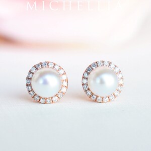 May include: A pair of pearl earrings with a diamond halo setting. The earrings are made of rose gold and feature a white pearl in the center of each earring.