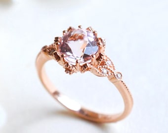 Puede incluir: Un delicado anillo de oro rosa con una piedra preciosa rosa engastada en un diseño floral. El anillo está adornado con pequeños diamantes.